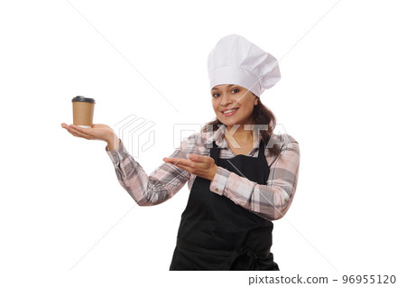 Pretty woman bartender barista waitress, wearing a white chef's hat and black apron, selling hot coffee drink in cardboard cup, smiling a toothy smile looking at camera, isolated on white background Pretty woman bartender barista waitress, wearing a white chef's hat and black apron, selling hot coffee drink in cardboard cup, smiling a toothy smile looking at camera, isolated on white background 96955120
