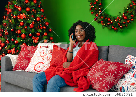 Young african woman talking on the smartphone sitting by christmas tree at home 96955781
