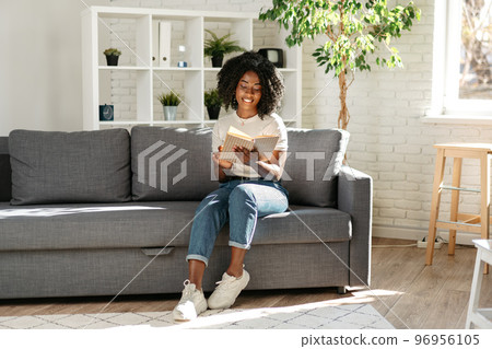 African woman reading book at home sitting on sofa African woman reading book at home sitting on sofa 96956105