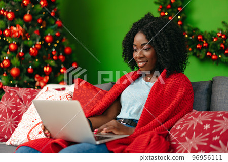 Beautiful african woman working with laptop on couch at home on Christmas Eve Beautiful african woman working with laptop on couch at home on Christmas Eve 96956111