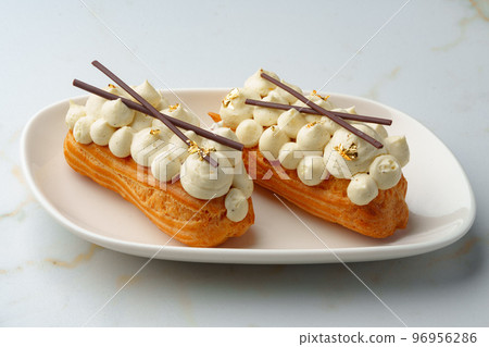 Two eclairs with white custard on whhite plate Two eclairs with white custard on whhite plate 96956286