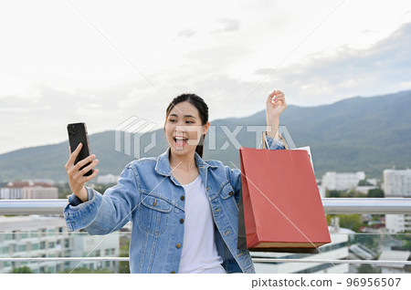 Asian woman using smartphone while carrying shopping bags Asian woman using smartphone while carrying shopping bags 96956507