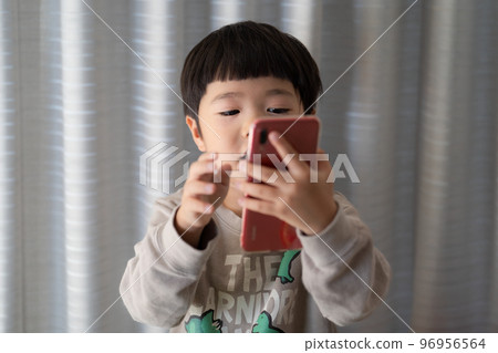 一個 5 歲男孩邊操作智能手機邊說話 96956564