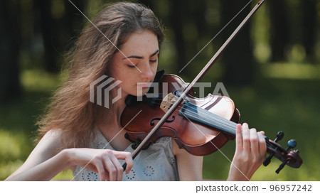A young girl plays the violin in the city park. A young girl plays the violin in the city park. 96957242