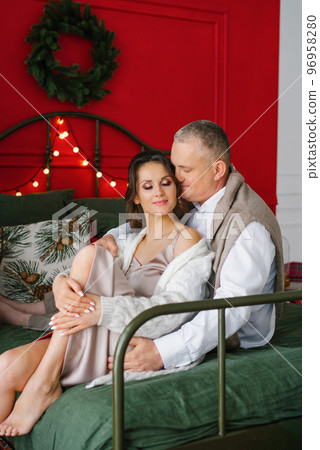 A couple in love is sitting on the bed by the Christmas tree and gently hugging 96958280