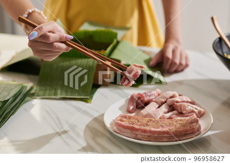 Woman adding pork pieces in mold covered with banana leaves 96958627