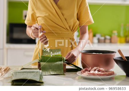 Woman putting banana leaves and rice in wooden mold when making square cake 96958633