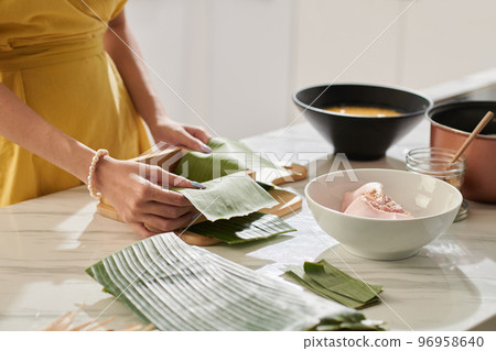 Hands of woman place cake in pot padded with dong leaf stalks when making square cake Hands of woman place cake in pot padded with dong leaf stalks when making square cake 96958640