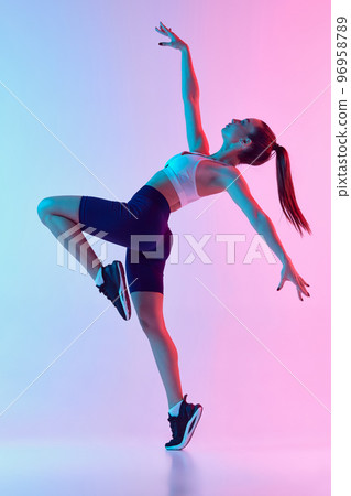 Portrait of young sportive woman training, doing full body exercises isolated over gradient blue pink background in neon light. Concept of sport, fitness, health 96958789
