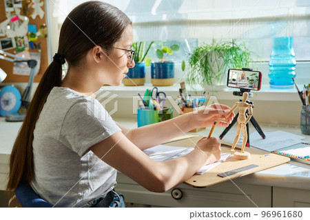 Teenage girl drawing sketch, looking at screen of smartphone 96961680