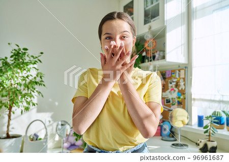 Surprised teenage girl covering mouth with hands looking at camera in home 96961687
