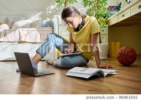 Teenage girl with glasses studying at home using a laptop Teenage girl with glasses studying at home using a laptop 96961692
