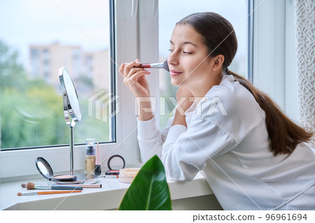 Young teenage girl with cosmetics mirror doing natural makeup, at home 96961694