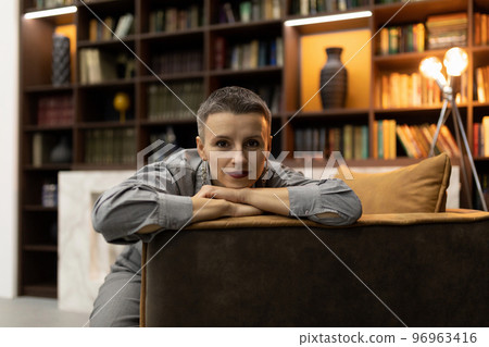 confident woman sitting in an armchair against the backdrop of a cozy home library confident woman sitting in an armchair against the backdrop of a cozy home library 96963416
