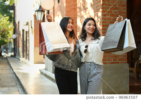 Two trendy beautiful women with shopping bags walking alone city street. Shopping, tourism and lifestyle concept 96963507