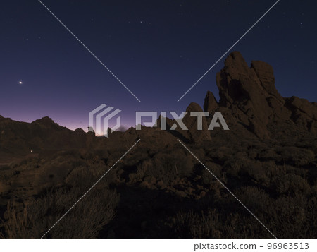 Long exposure night shot of Roques de Garcia volcanic rock formation at El Teide national park, early night winter sky with stars on pink blue glow. Tenerife Canary islands, Spain 96963513