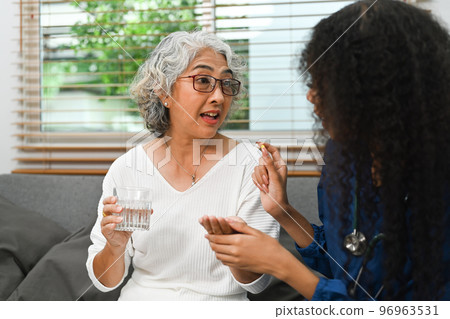Healthcare worker or nurse caregiver giving pills, showing a prescription drug to senior woman. Elderly healthcare concept 96963531