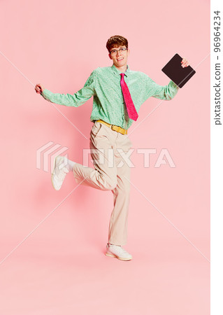 Funny emotional man, student geek wearing vintage style shirt and trousers having fun, using tablet isolated over light pink background. Fun, style, fashion, emotions 96964234
