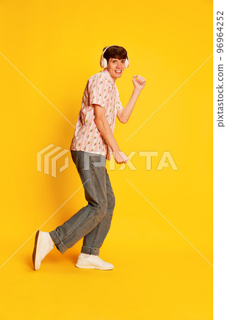Emotional smiling man, student in headphones listening to music and dancing isolated over bright yellow background. Music, happiness, fun, joy Emotional smiling man, student in headphones listening to music and dancing isolated over bright yellow background. Music, happiness, fun, joy 96964252