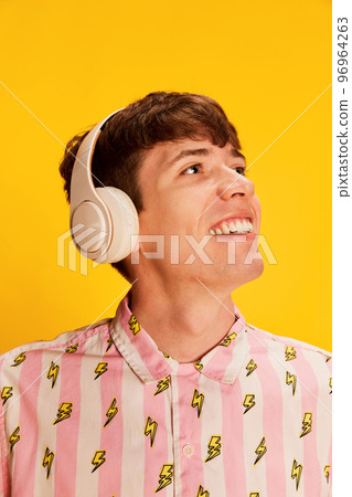 Closeup portrait of emotive young man in headphones smiling, listening to music isolated over bright yellow background. Youth culture, positive emotions 96964263
