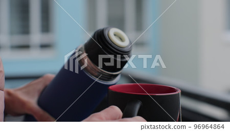 A woman pours herbal tea from a thermos, close-up. 96964864
