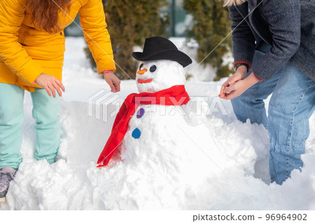Two faceless Caucasian women are making a snowman. Winter fun. 96964902