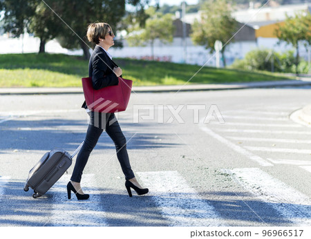 Businesswoman with trolley bag walking in urban environment. Wearing a red bag 96966517