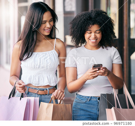 Women, friends and shopping with phone in city for mobile app connection, technology and internet. Happy customers, shopping bags and search social media for discount stores, fashion sales and market 96971180