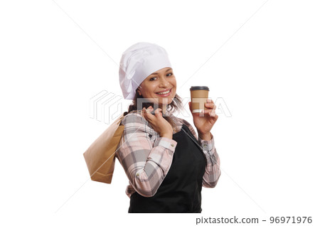 Side portrait, smiling positive woman waitress in chef hat and apron, posing with recyclable paper bag and takeaway hot drink, isolated on white background. Food and drink delivery and consumerism Side portrait, smiling positive woman waitress in chef hat and apron, posing with recyclable paper bag and takeaway hot drink, isolated on white background. Food and drink delivery and consumerism 96971976