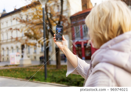 Woman takes photo on her smartphone on excursion. Hand close-up. Back view. Concept of social media and online communication Woman takes photo on her smartphone on excursion. Hand close-up. Back view. Concept of social media and online communication 96974021