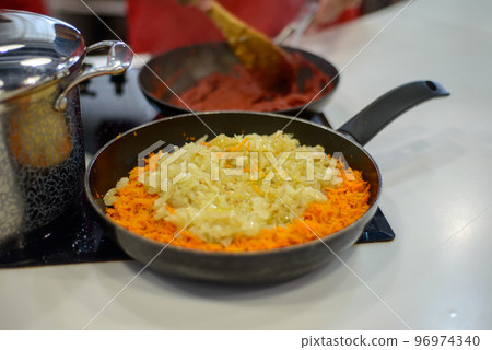 carrots and onions are fried or stewed on an electric stove in a black frying pan 96974340