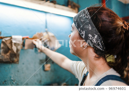 Gender equality. Portrait of a young woman in uniform working in a workshop, which attaches a piece of paper with a record on the wall. Background is blur. Close up 96974601
