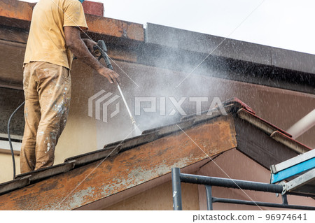 Worker using high pressure water jet spray gun to wash and clean dirt from rooftop tiles in renovation 96974641