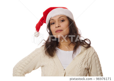 Isolated portrait on white background of a multi-ethnic beautiful brunette woman, wearing Santa hat and warm knitted beige sweater, looking at camera with an insightful look. Copy advertising space Isolated portrait on white background of a multi-ethnic beautiful brunette woman, wearing Santa hat and warm knitted beige sweater, looking at camera with an insightful look. Copy advertising space 96976171