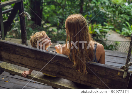 Mom and son on a swing in a tropical garden 96977374