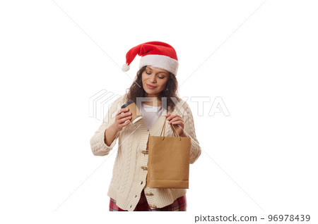 Latin American pretty woman in Santa hat and beige warm sweater, unpacking a takeaway hot drink, tea or coffee from paper bag, enjoys food delivery at Christmas time, isolated over white background 96978439