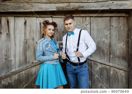 A hipster couple stands and smiles against the backdrop of an old wooden fence. A hipster couple stands and smiles against the backdrop of an old wooden fence. 96978649