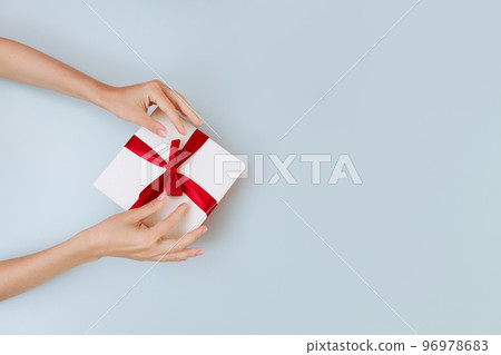 Women's hands hold a white with a red ribbon bow Women's hands hold a white with a red ribbon bow 96978683