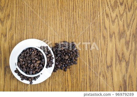 Cup of coffee in a white cup and coffee beans on wooden table background, top view. Cup of coffee in a white cup and coffee beans on wooden table background, top view. 96979289