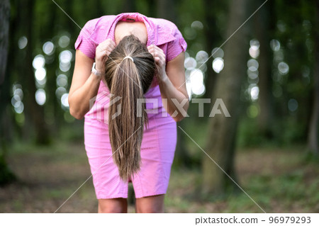 Creepy woman with long hair standing bent down in moody dark forest. 96979293