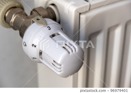 Closeup of heating radiator valve for comfortable temperature regulation on metal radiator on inrerior wall. 96979401