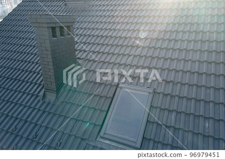 Closeup of attic window and brick chimney on house roof top covered with ceramic shingles. Tiled covering of building Closeup of attic window and brick chimney on house roof top covered with ceramic shingles. Tiled covering of building 96979451
