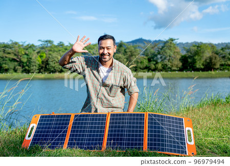 Asian man sit behide solar cells panel and wave hand with smiling to camera and he stay near lake 96979494