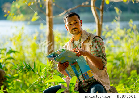 Asian man hold map and sit in the forest with relax during travel and camping in national park. Asian man hold map and sit in the forest with relax during travel and camping in national park. 96979501