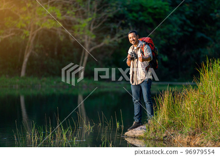 Smart man with backpack accessories look at camera and show thumbs up also stand near lake 96979554