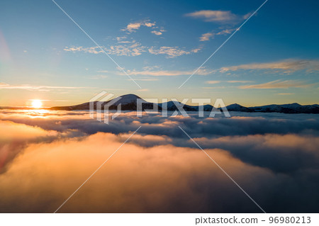 Aerial view of vibrant sunrise over white dense fog with distant dark Carpathian mountains on horizon. Aerial view of vibrant sunrise over white dense fog with distant dark Carpathian mountains on horizon. 96980213