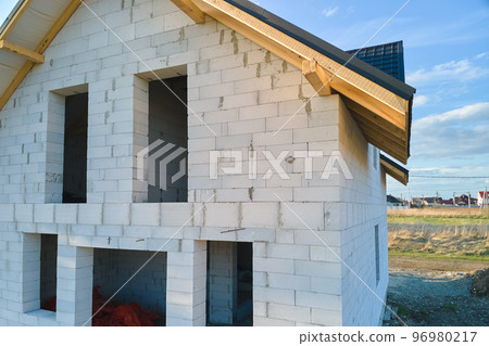 Aerial view of unfinished house with aerated lightweight concrete walls and wooden roof frame covered with metallic tiles under construction. 96980217