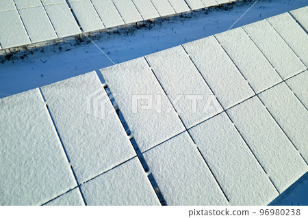Aerial view of snow covered sustainable electric power plant with rows of solar photovoltaic panels for producing clean electrical energy. Low effectivity of renewable electricity in northern winter 96980238