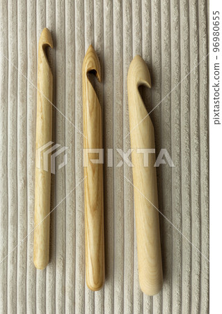 Assorted wooden knitting needles lie on a wooden table, in the background a blurred gray plaid merino wool 96980655
