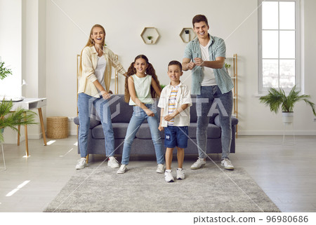 Happy family of four is having fun dancing to music in living room of bright apartment. 96980686
